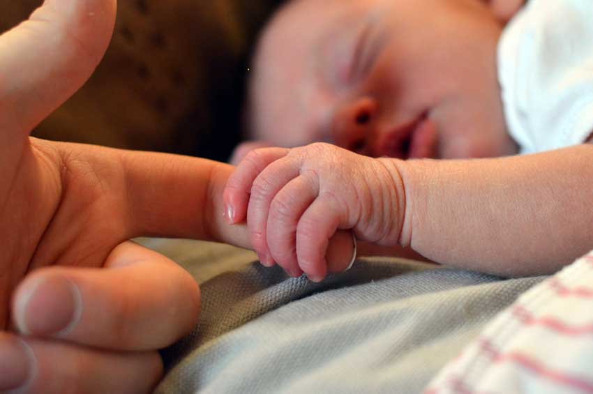 baby grabbing adult's finger in early days of life