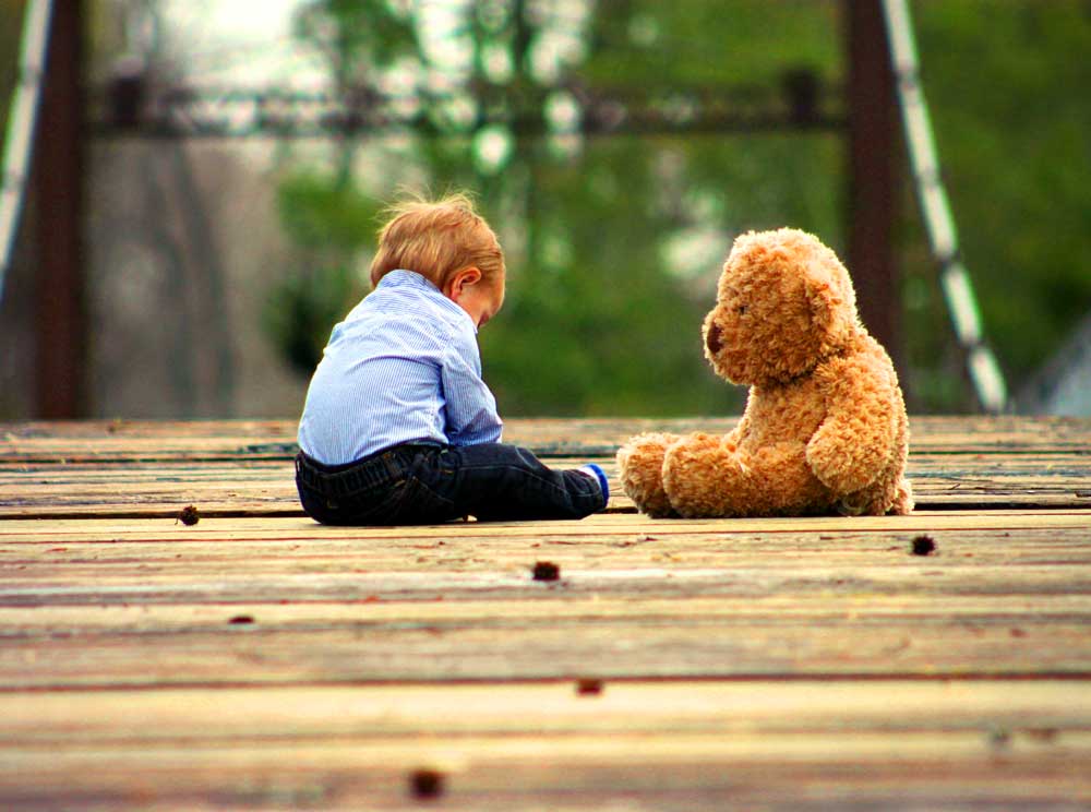 boy sits on deck with a teddy bar