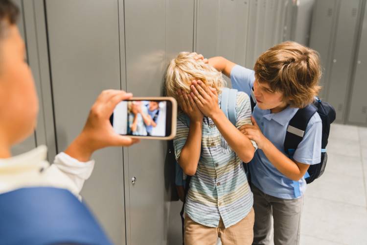 boy bullying other boy in hallway while someone records on smartphone