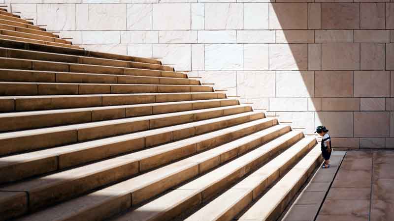 a toddler child stands at the bottom of imposing stone staircase