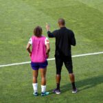coach talks to player on soccer pitch