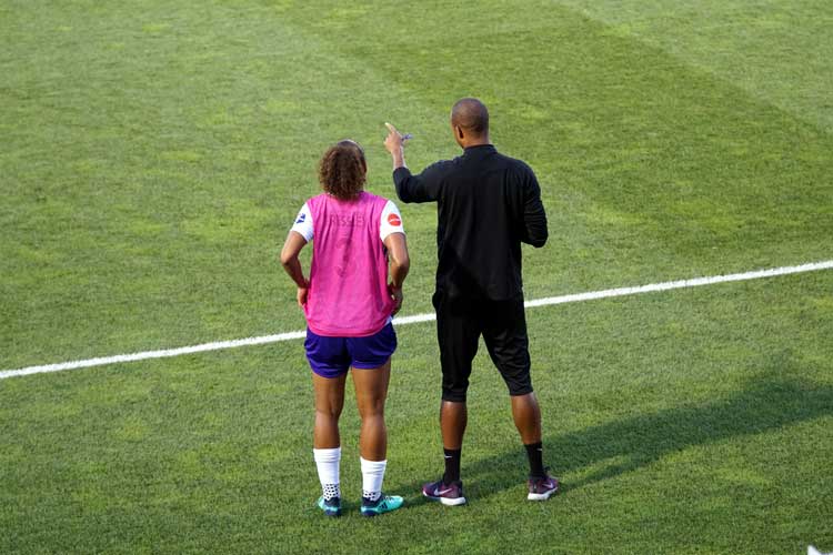 coach talks to player on soccer pitch