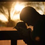 father snuggles baby in silhouette as sun rises behind them
