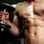 man with ripped abs lifts dumbbell at home gym