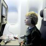 child in airplane seat watching screen