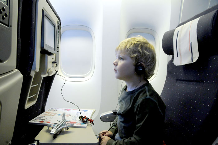 child in airplane seat watching screen